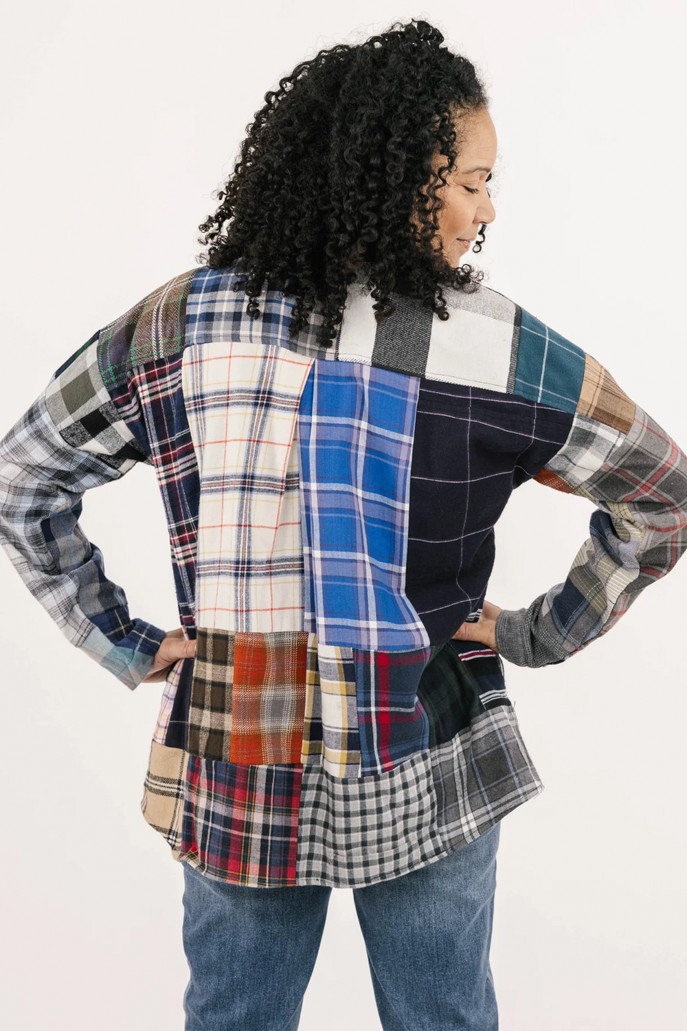 A woman standing in front of a light grey background wearing a plaid patchwork shirt. 
