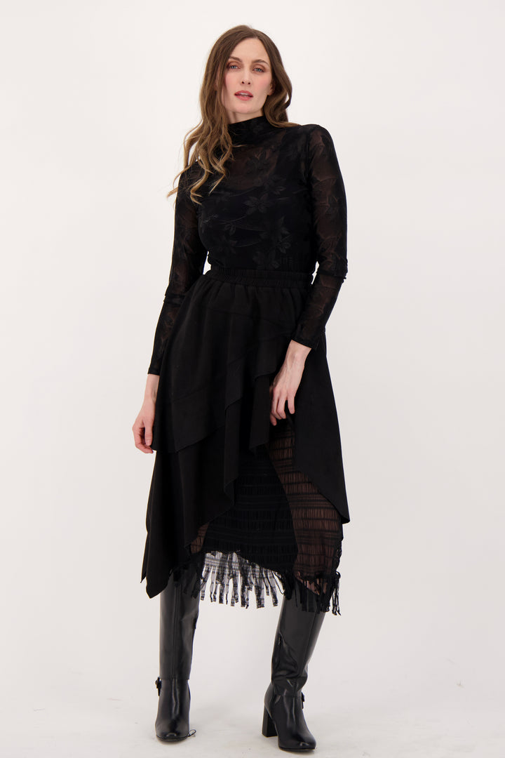 A woman modelling a sheer floral lace long sleeve top and black skirt in front of a white background. 