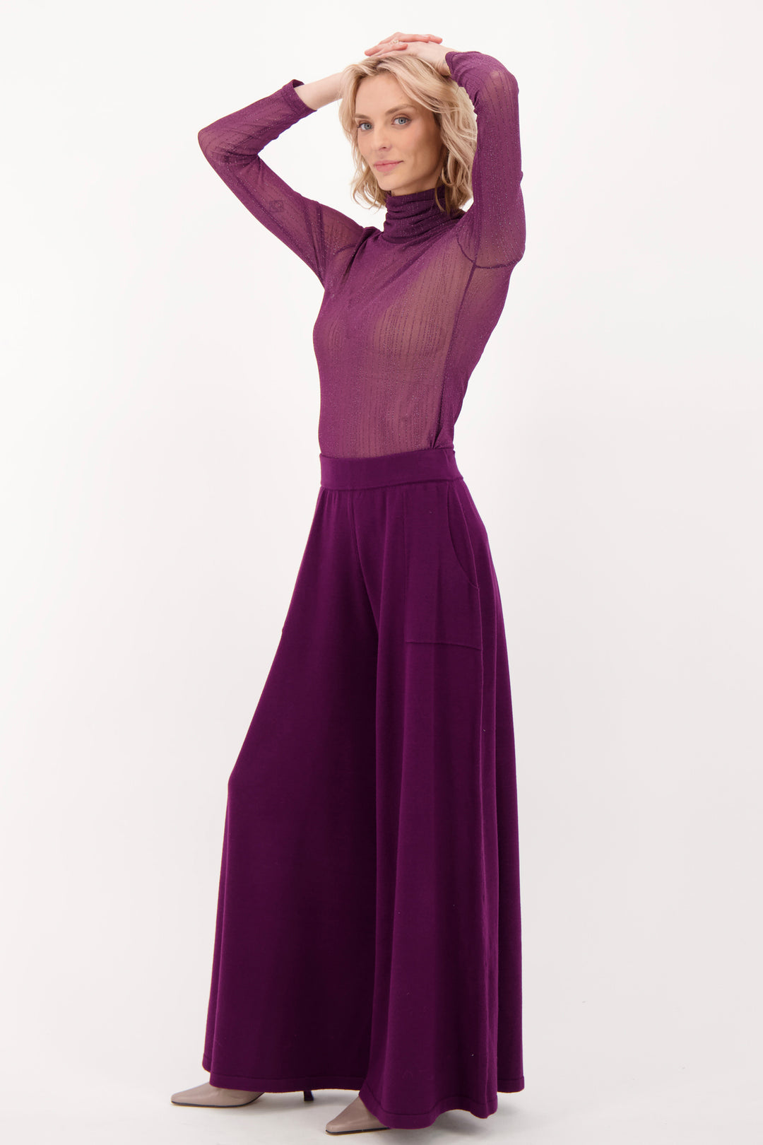 A woman modelling a sheer purple long sleeve top and pants in front of a white background. 
