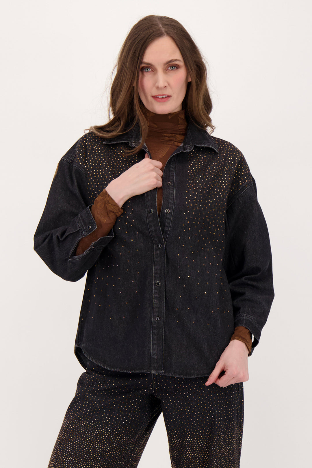 A woman modelling a black denim shirt with falling bronze embellishments in front of a white background. 