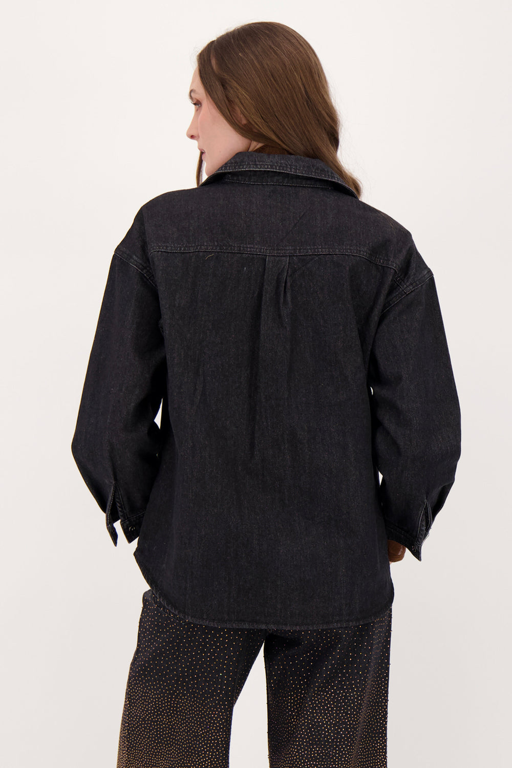 A woman modelling a black denim shirt with falling bronze embellishments in front of a white background. 