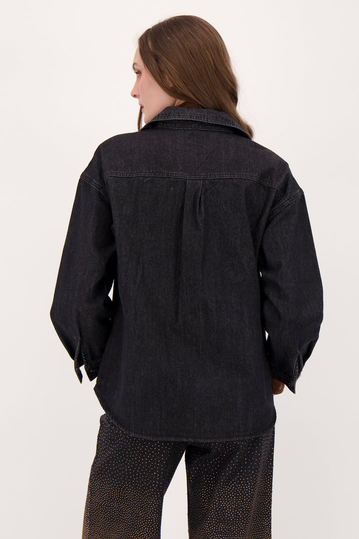 A woman modelling a black denim shirt with falling bronze embellishments in front of a white background. 