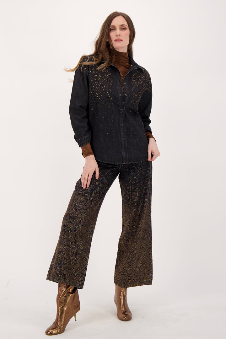 A woman modelling a black denim shirt with falling bronze embellishments in front of a white background. 