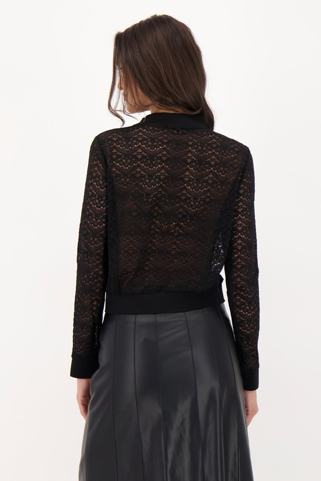 A woman modelling a black lace long sleeve top and pleather skirt in front of a grey background. 