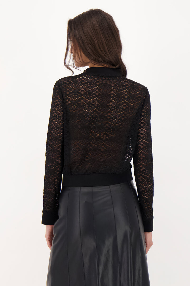 A woman modelling a black lace long sleeve top and pleather skirt in front of a grey background. 