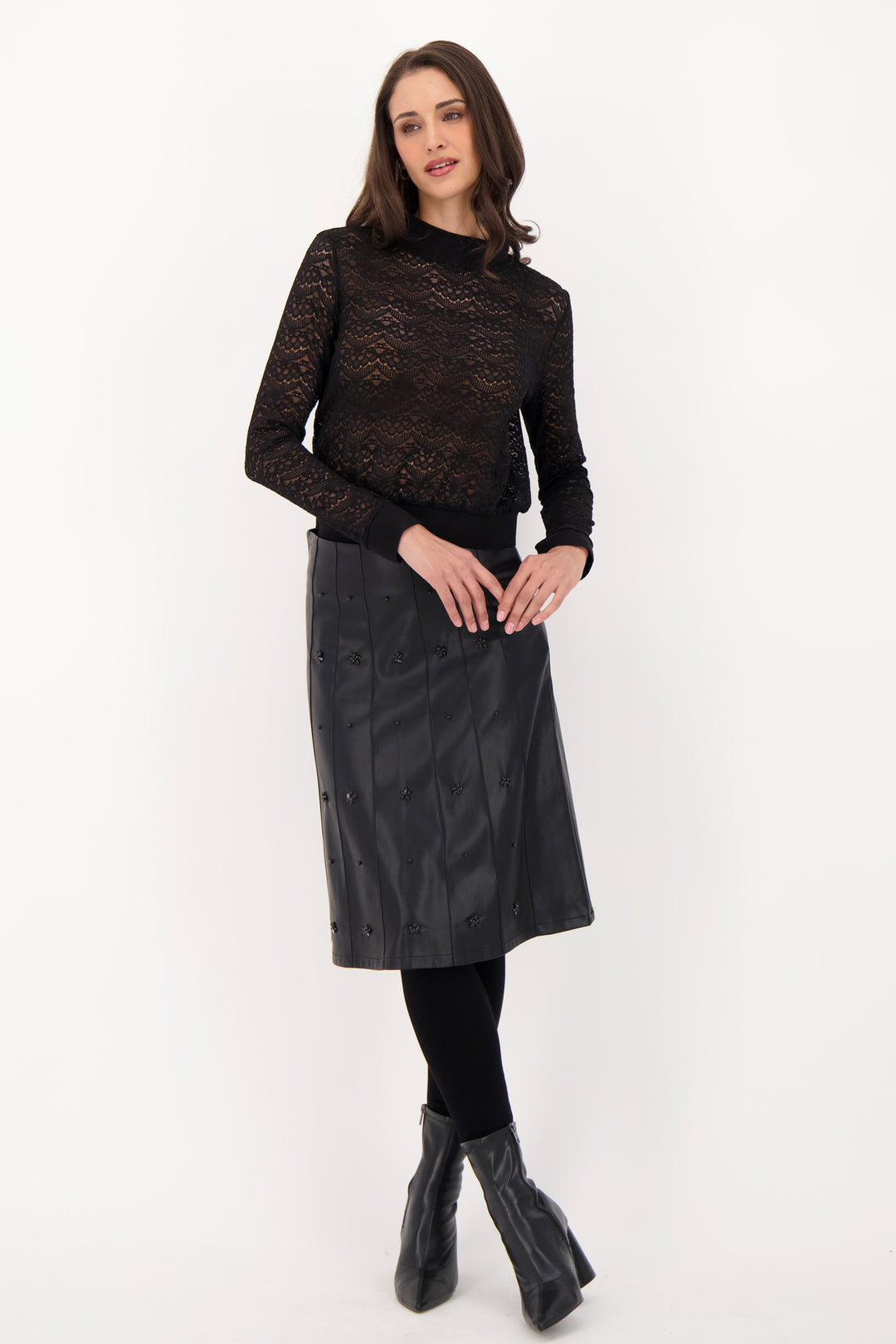 A woman modelling a black lace long sleeve top and pleather skirt in front of a grey background. 