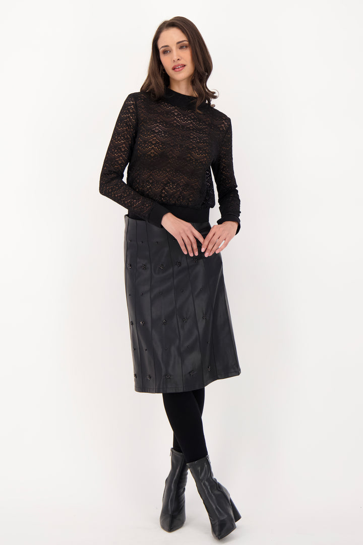A woman modelling a black lace long sleeve top and pleather skirt in front of a grey background. 
