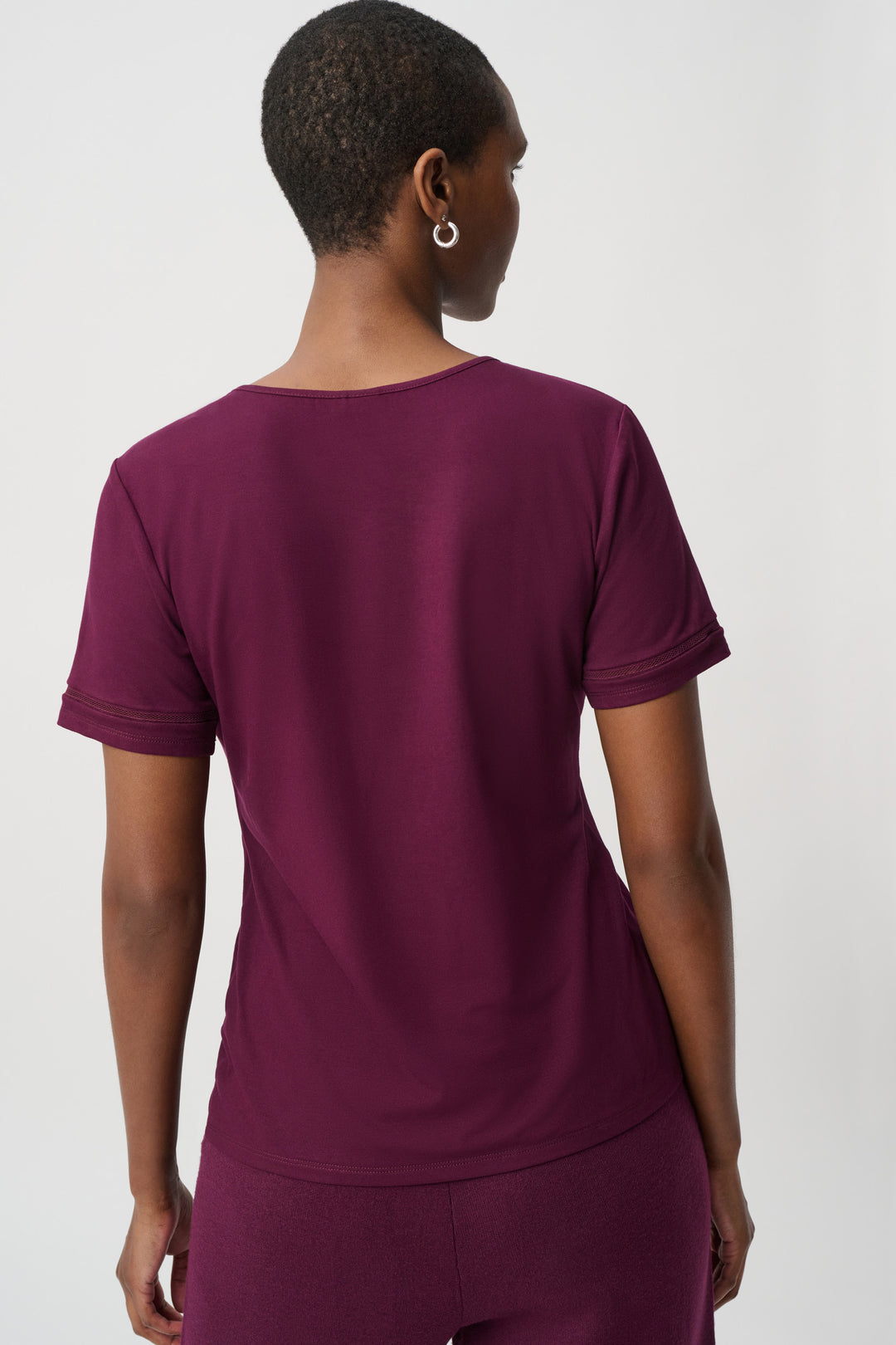 A woman shown from the back modelling a burgundy short sleeve t-shirt standing in front of a light grey background. 