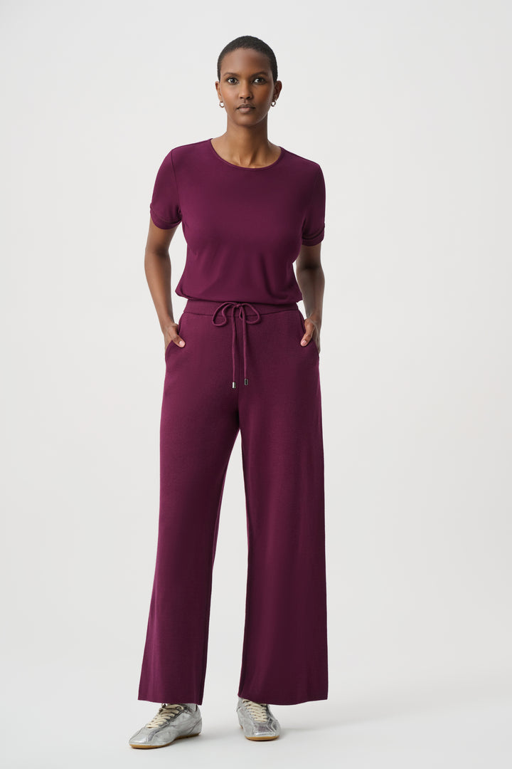 A woman modelling a burgundy short sleeve t-shirt standing in front of a light grey background. 