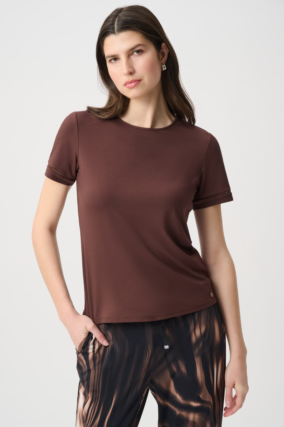 A woman modelling a brown short sleeve t-shirt standing in front of a light grey background. 