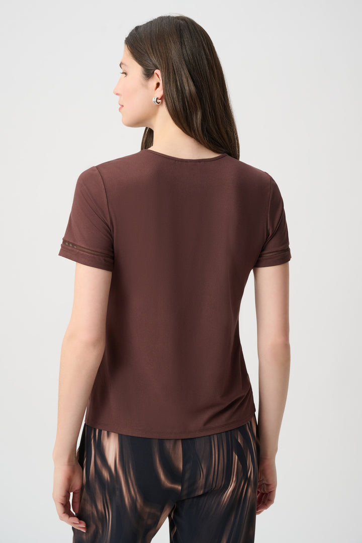 A woman shown from the back modelling a brown short sleeve t-shirt standing in front of a light grey background. 