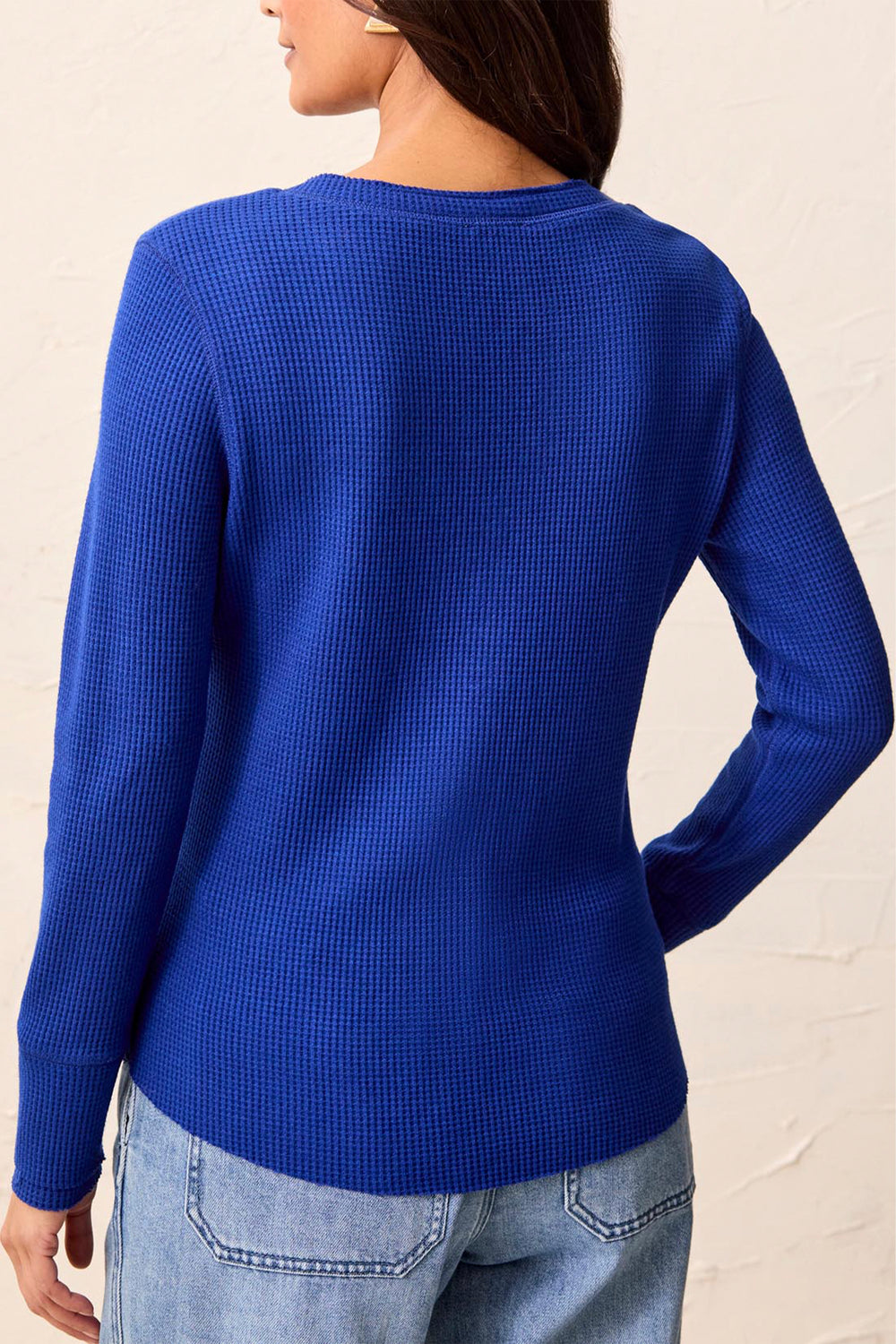 A woman shown from the back modelling a long sleeve waffle henley t-shirt standing in front of a beige background. 