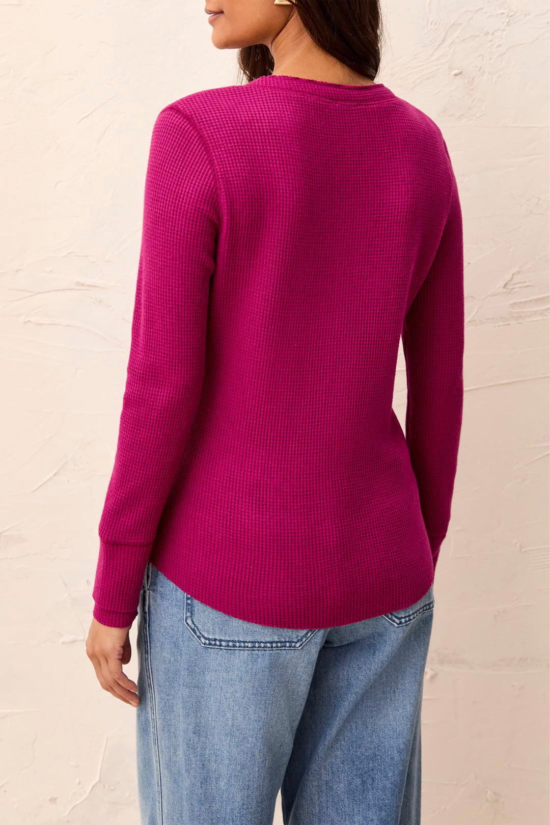 A woman shown from the back modelling a long sleeve waffle henley t-shirt standing in front of a beige background. 
