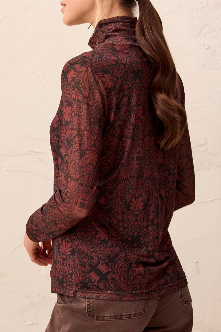 A woman shown from the back wearing a mock neck brown pattered long sleeve stop standing in front of a beige background. 