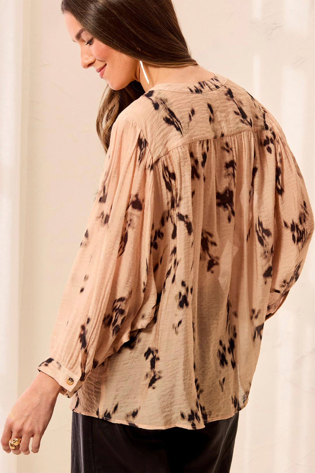 A woman shown from the back wearing an oversized loose blouse with floral print standing in front of a beige background. 