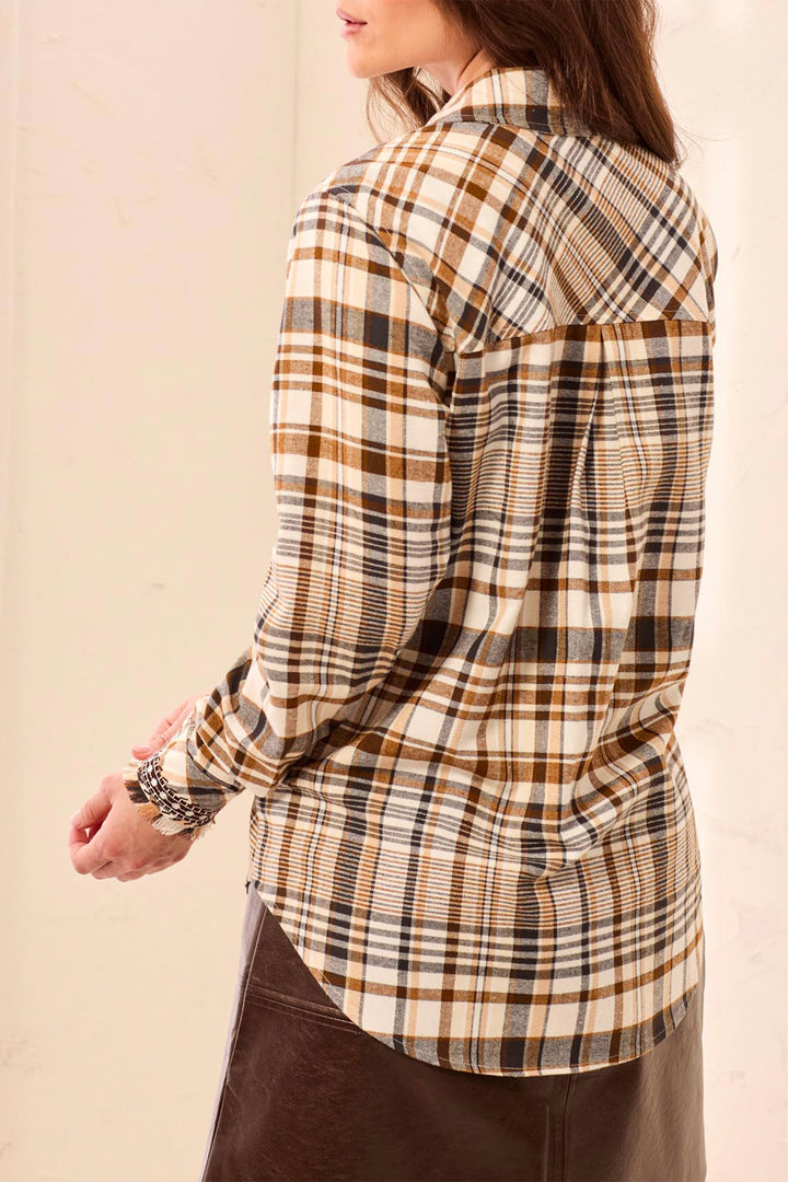 A woman shown from the back wearing a beige and brown plaid long sleeve shirt standing in front of a beige background. 
