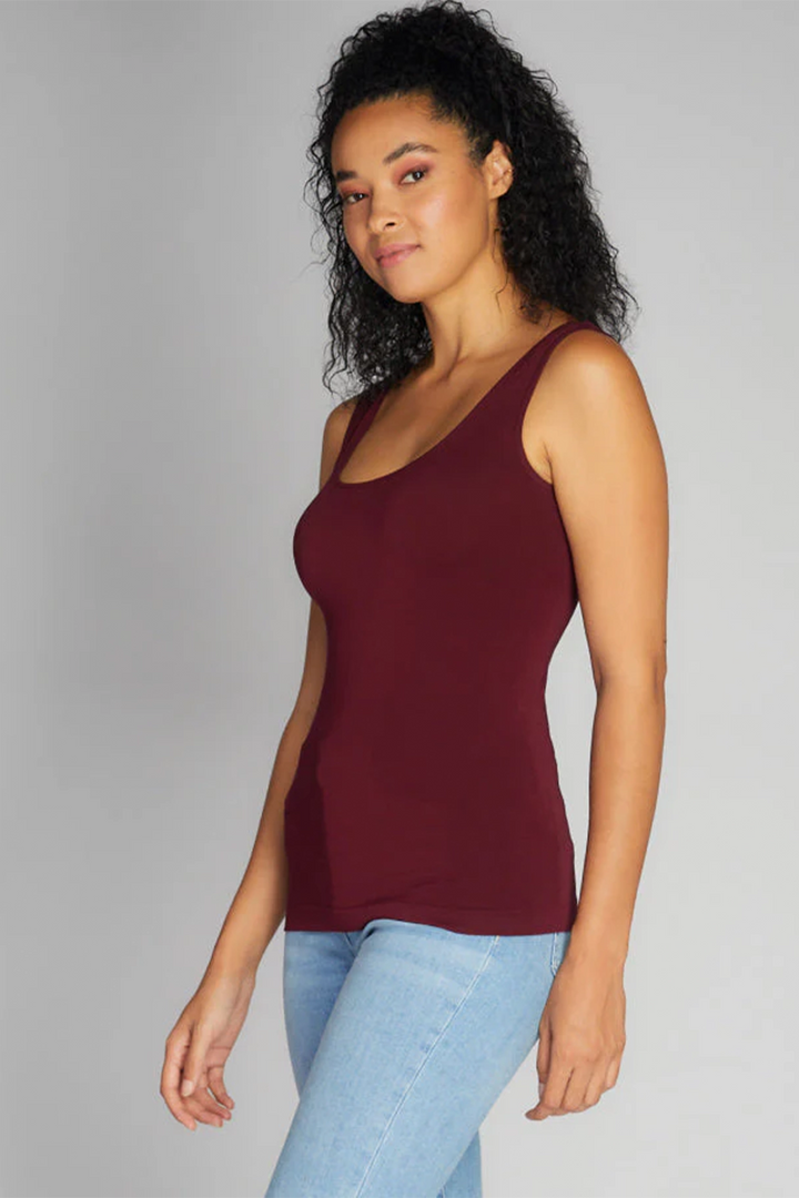 Woman wearing a burgundy tank top and light blue jeans against a gray background