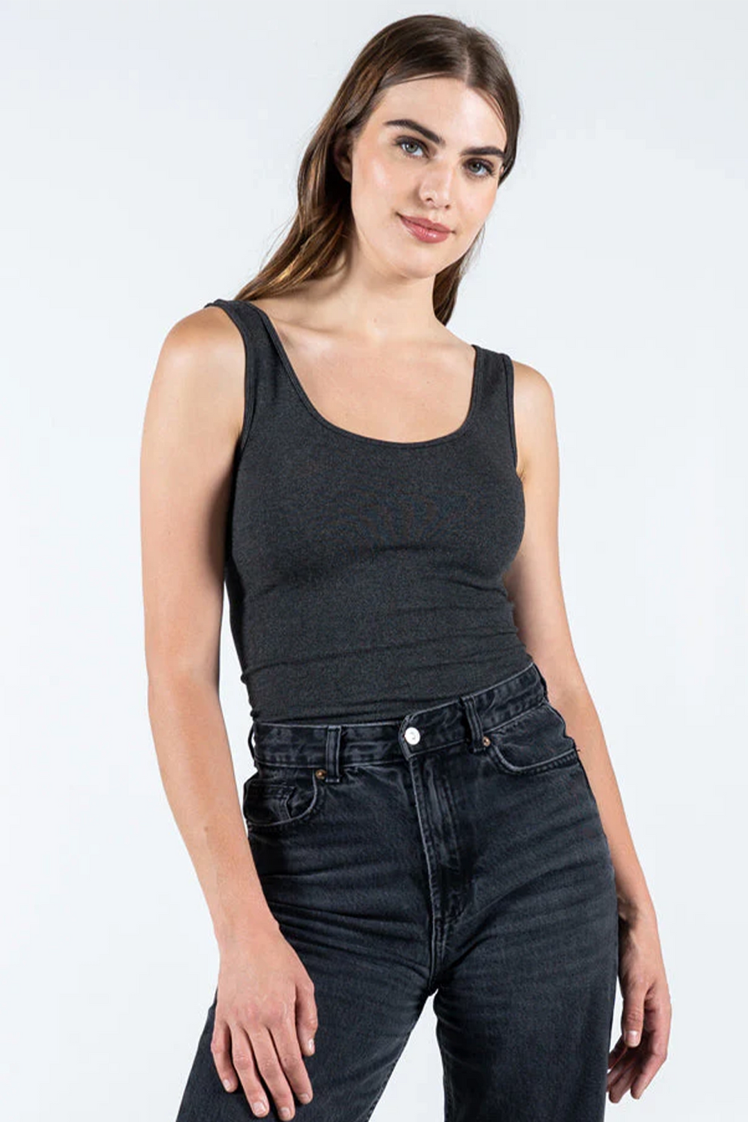 A woman wearing a black short tank top with wide straps and black jeans.