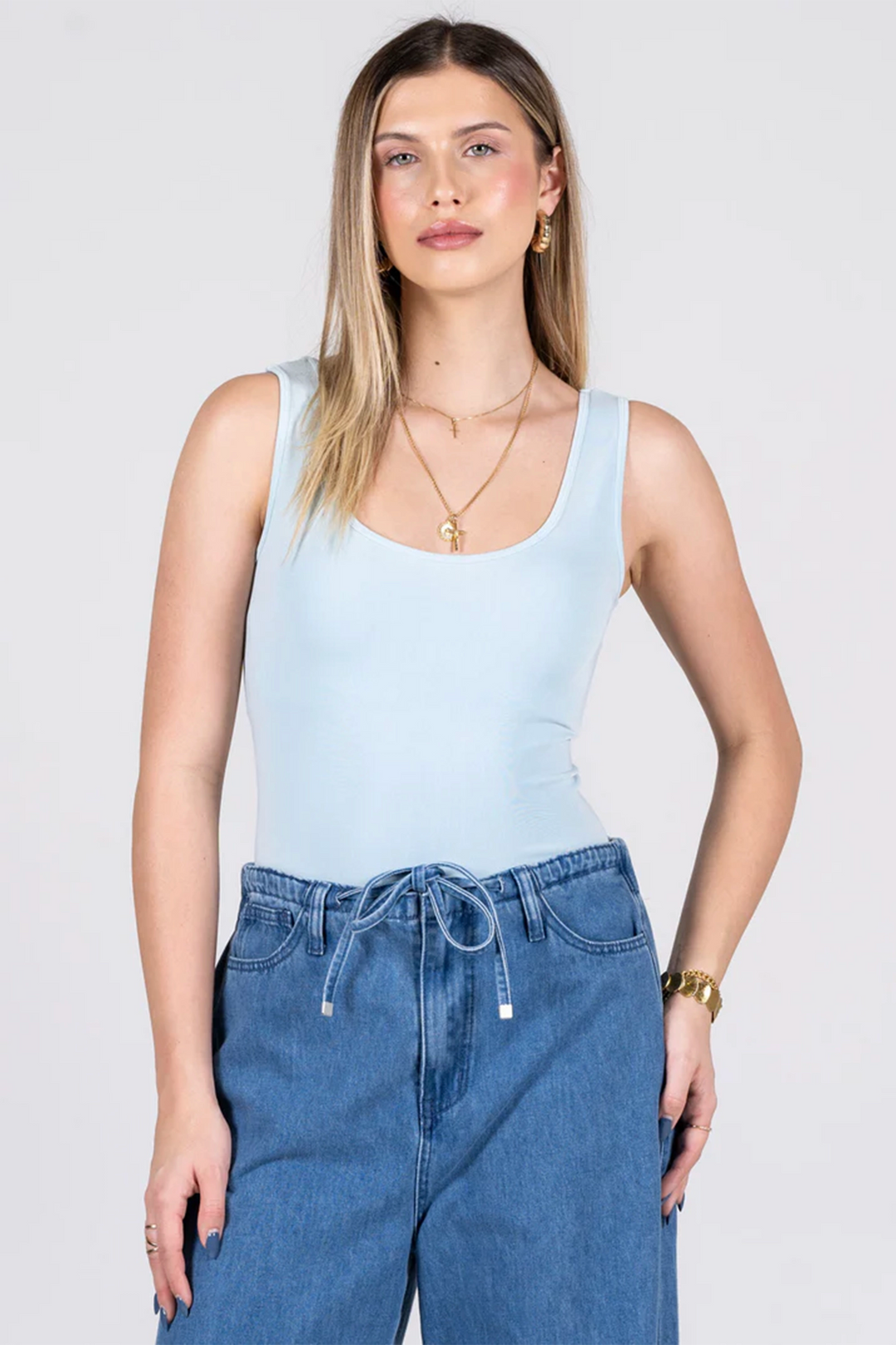 Woman wearing a light blue tank top and blue jeans on a white background