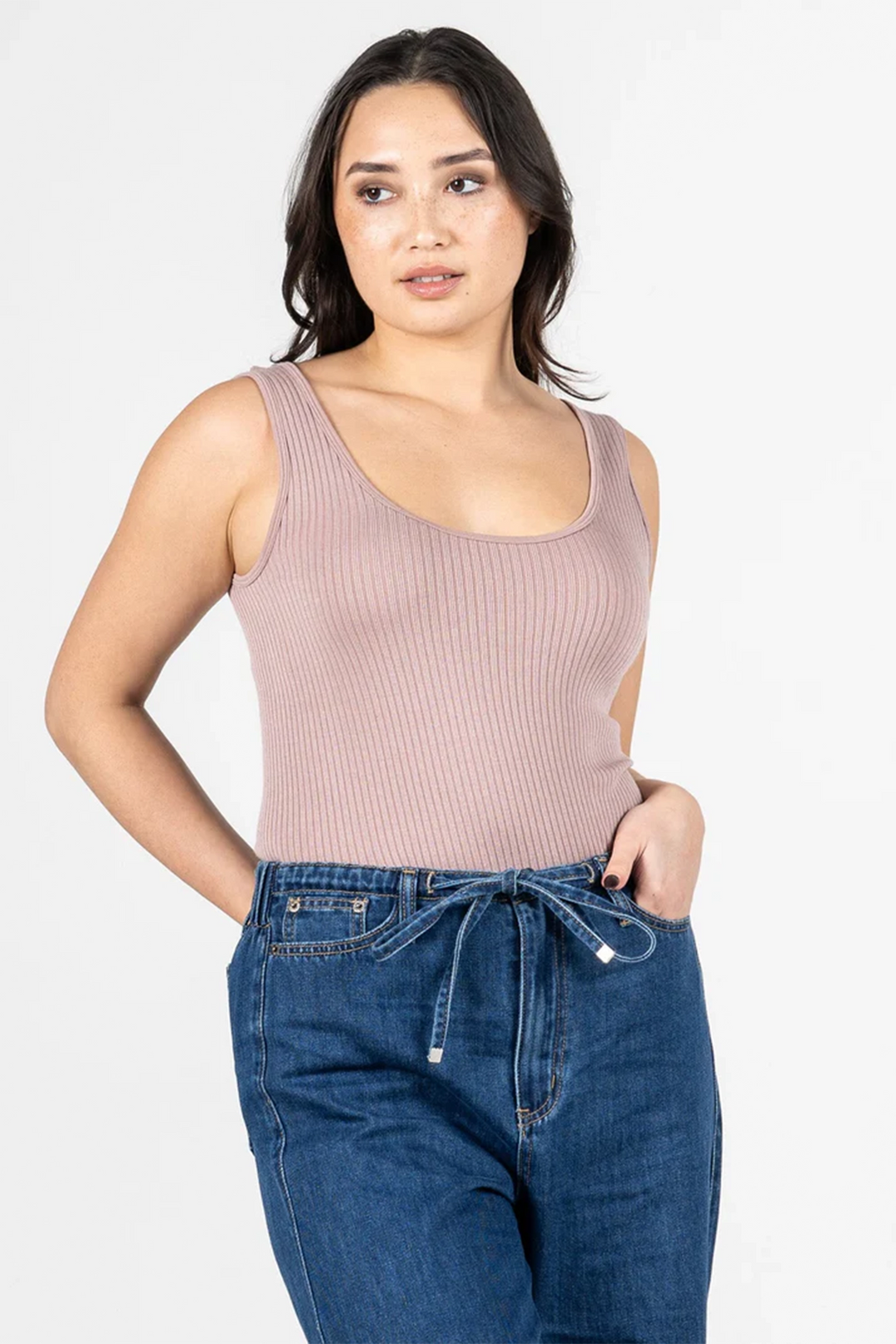 Woman wearing a light mocha brown ribbed tank top and blue jeans on a white background