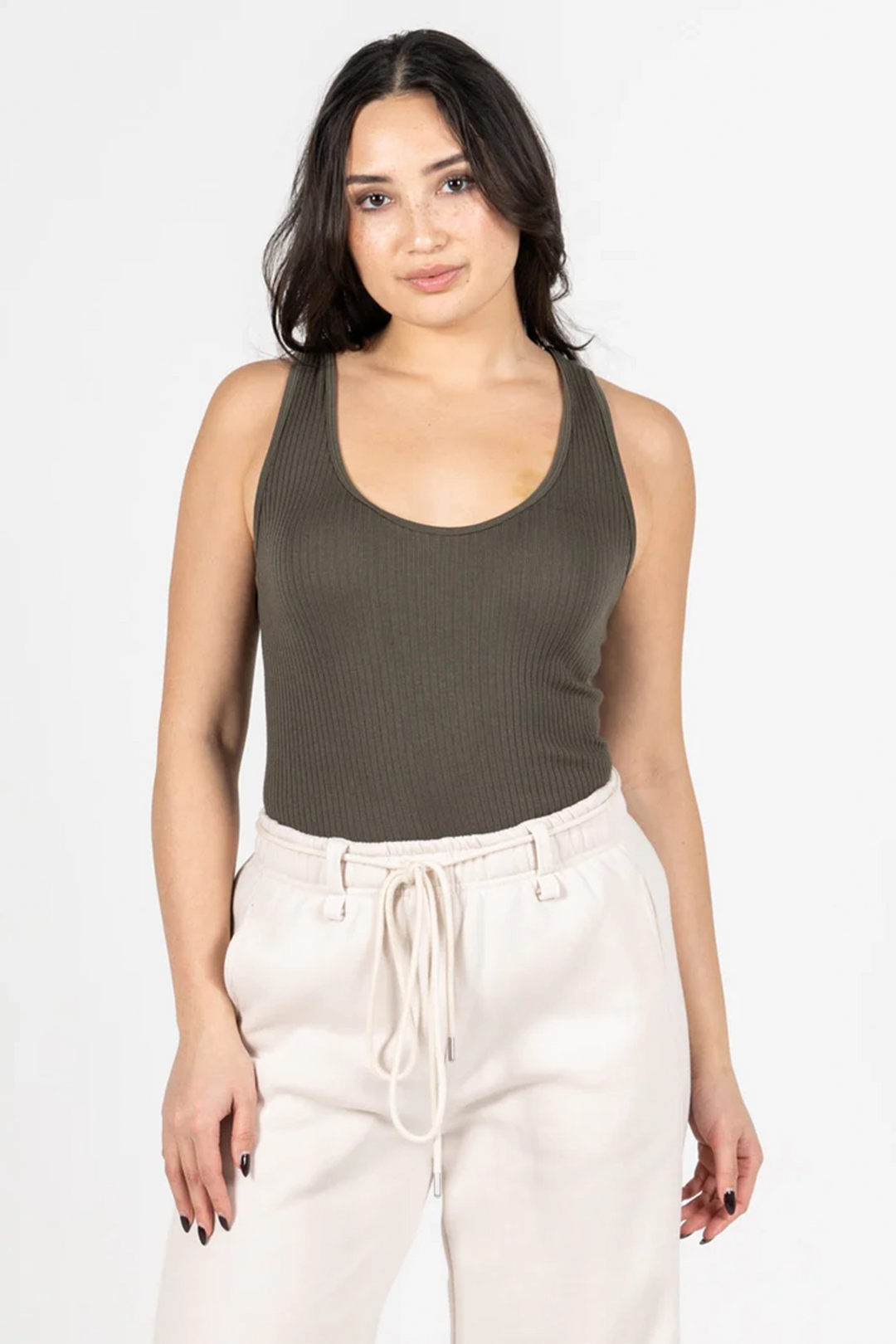 Woman wearing an olive green ribbed tank top and white pants on a white background
