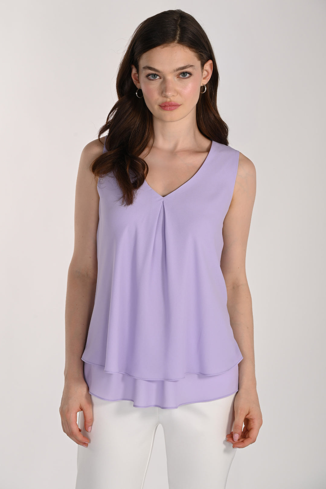 Women wearing a sleeveless layered blouse with white pants in front of beige background