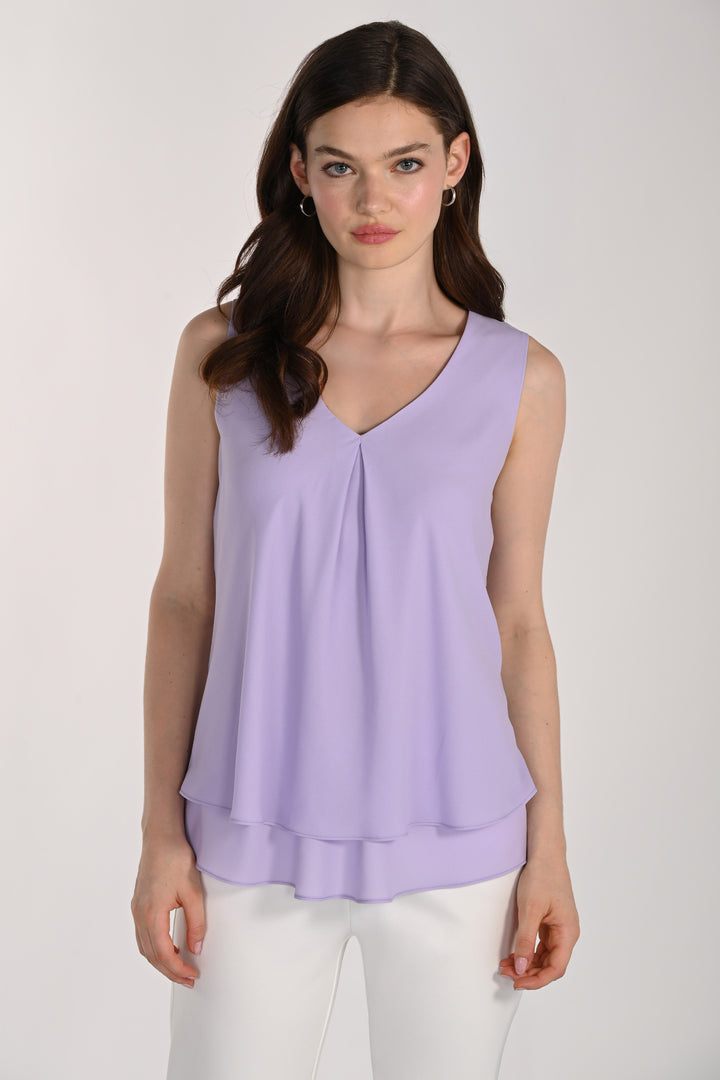 Women wearing a sleeveless layered blouse with white pants in front of beige background