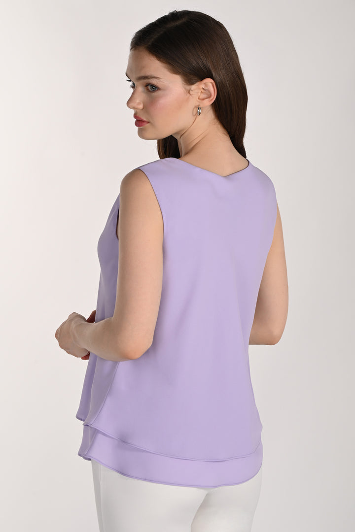 Women wearing a sleeveless layered blouse with white pants in front of beige background