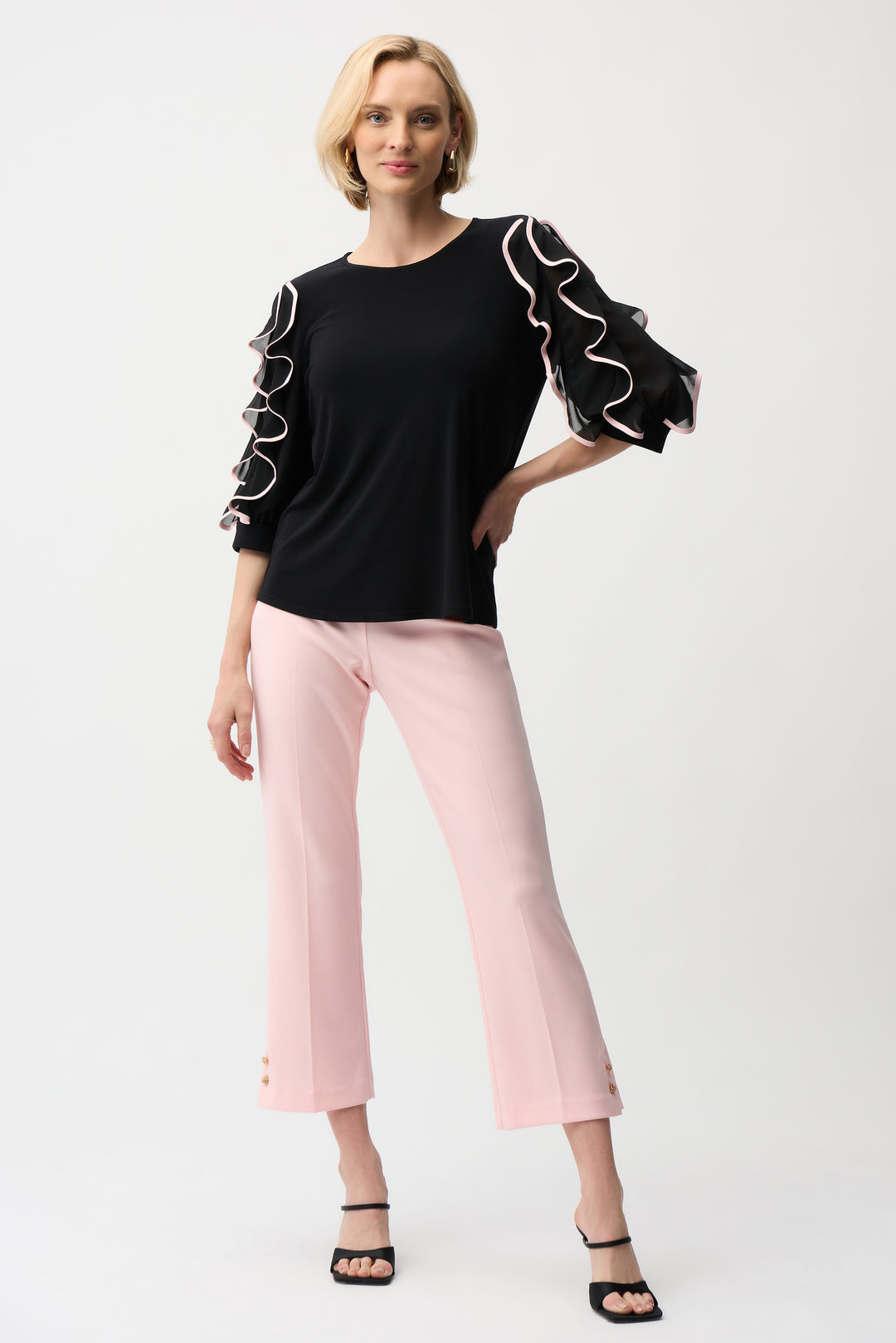 Woman wearing a black top with white ruffle sleeves and pink pants on a white background