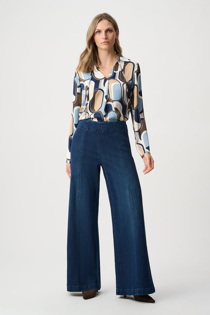 Woman wearing a patterned blouse and blue wide-leg pants on a white background
