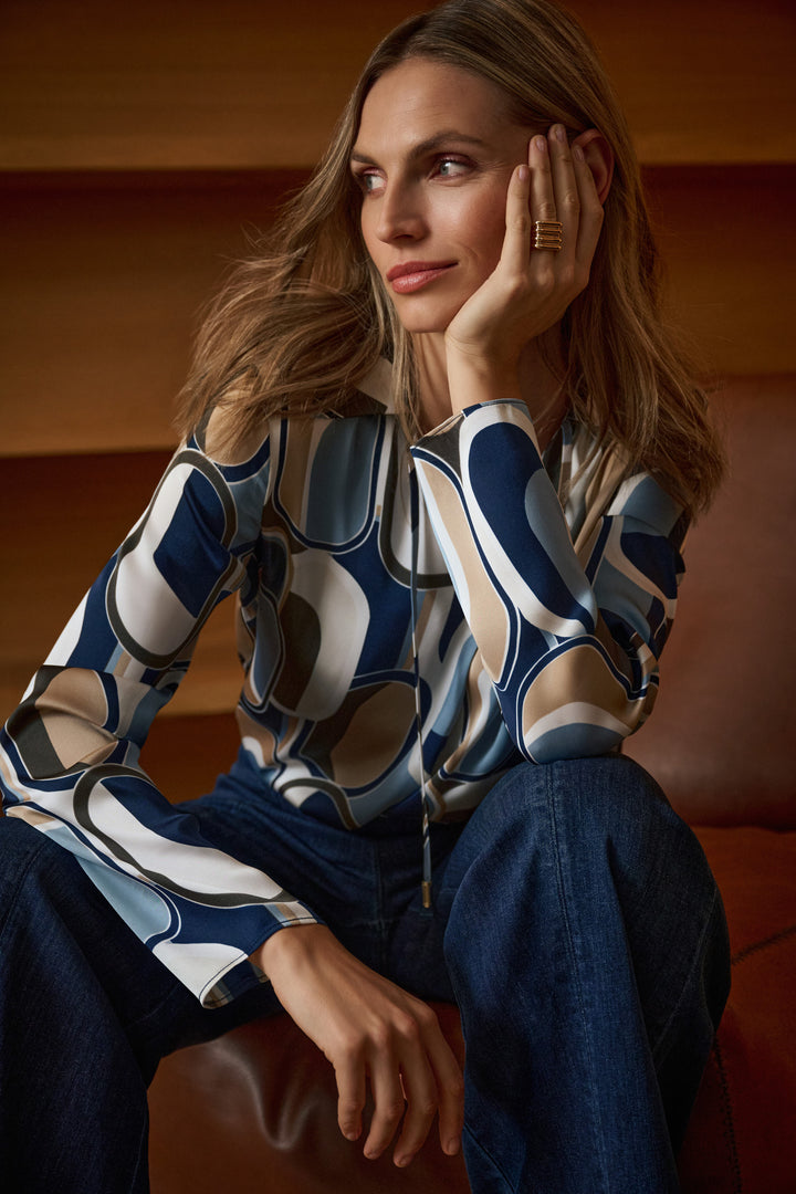 Woman wearing a patterned top sitting on a couch with a warm-toned background
