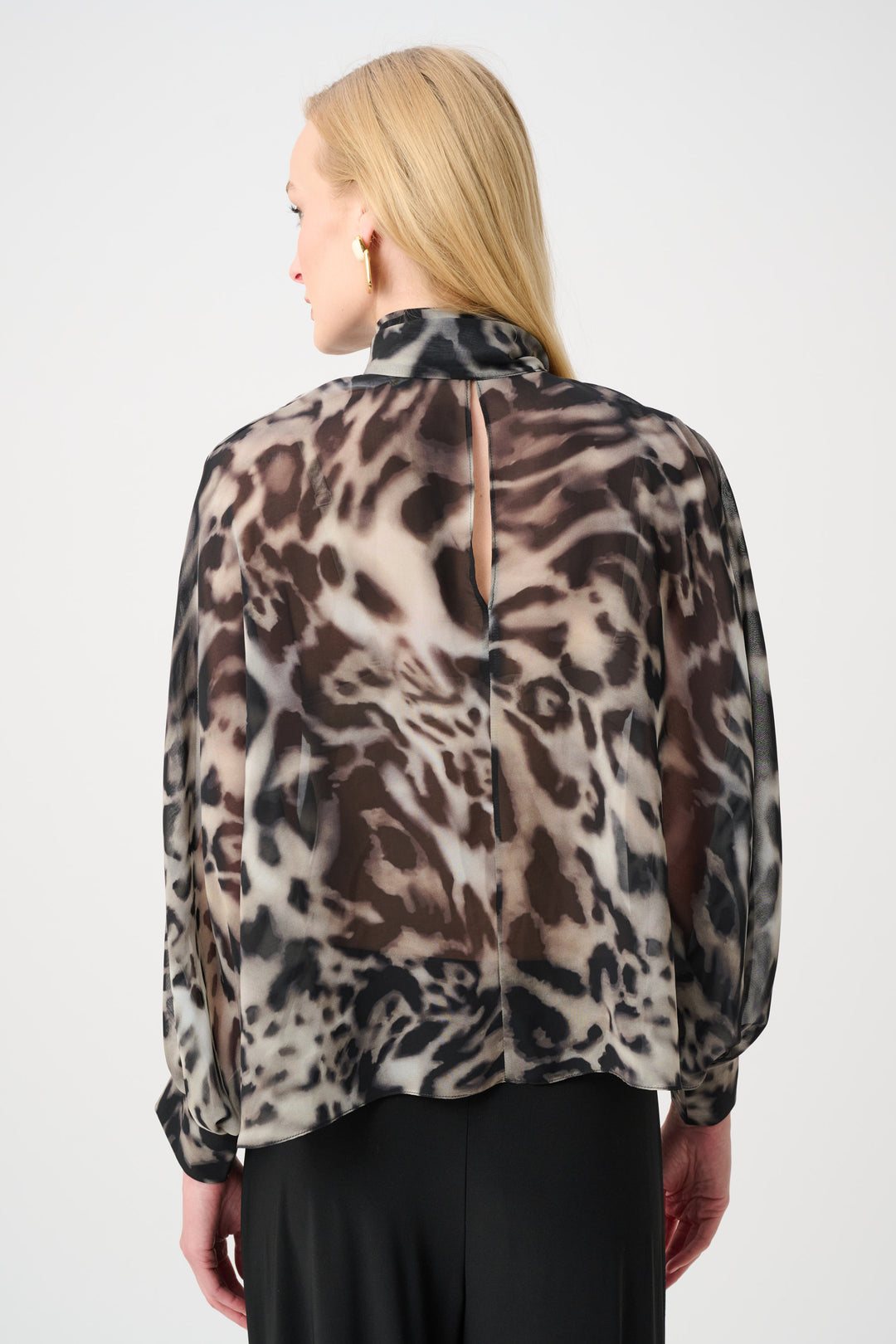 A woman shown from the back modelling an animal print blouse with black pants standing in front of a light grey background. 