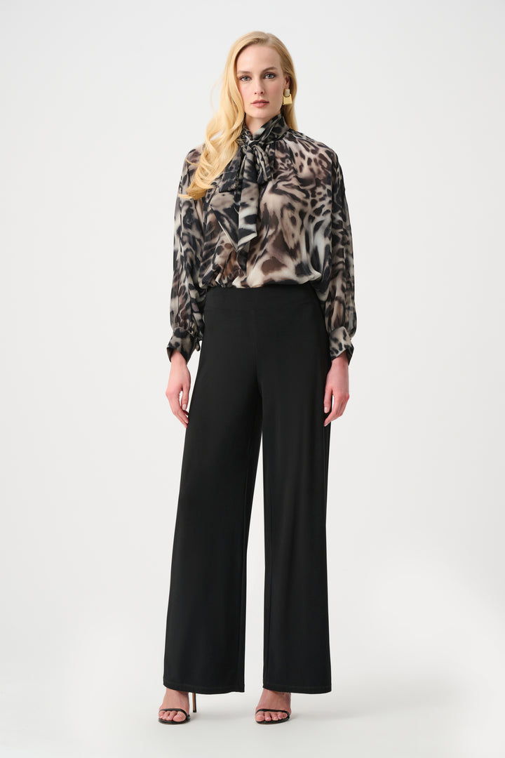 A woman modelling a animal print blouse with black pants standing in front of a light grey background. 