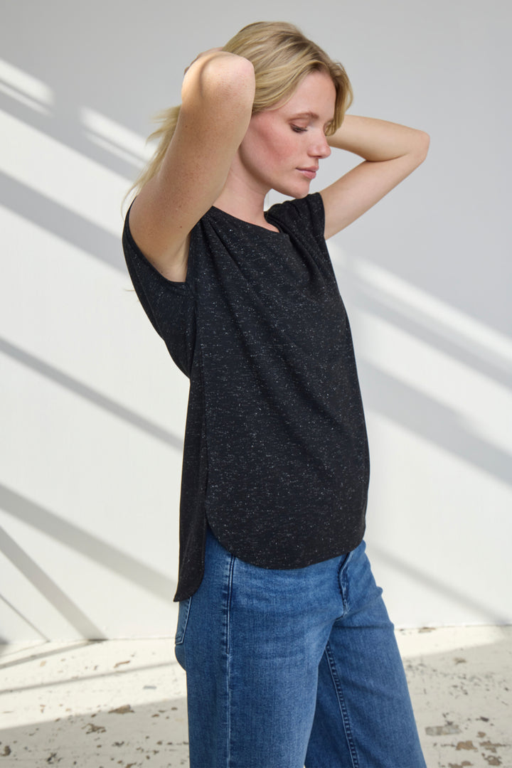 Woman wearing a black top and blue jeans against a white wall.