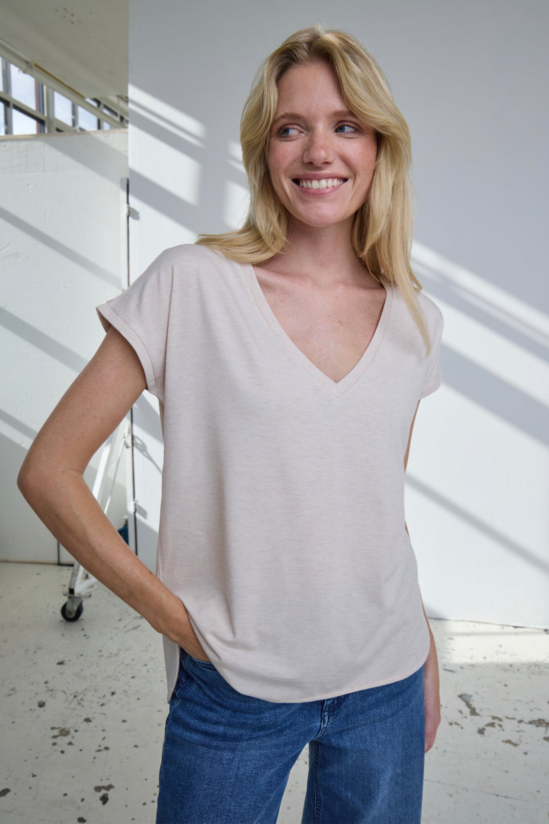 Woman wearing a light-colored top and blue jeans standing indoors.
