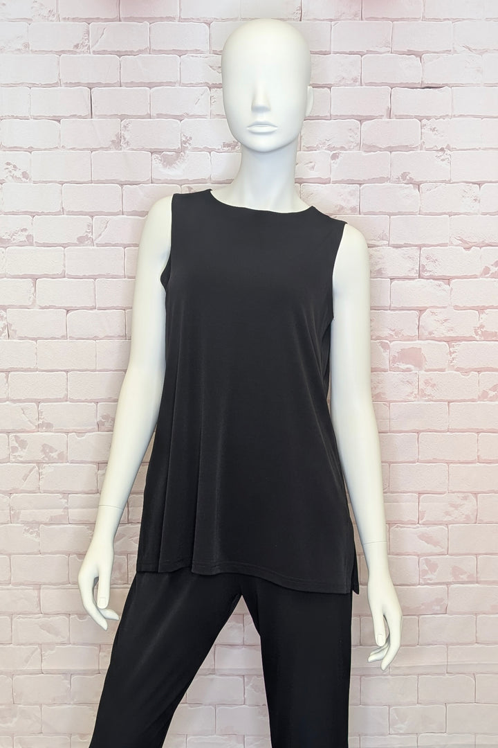 Mannequin wearing a black sleeveless top and pants against a light brick wall.