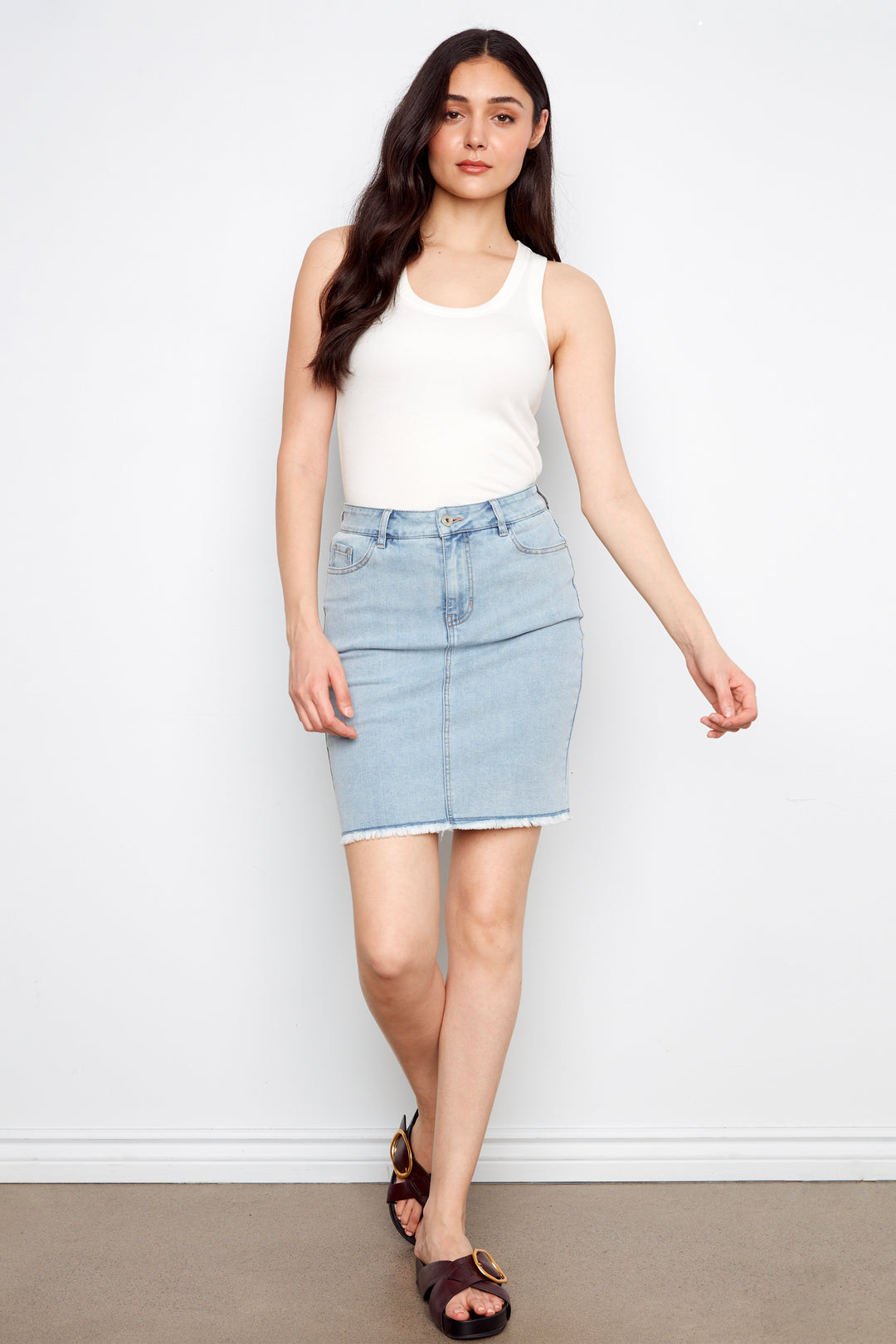 Woman wearing a white tank top and light blue denim skirt against a white background