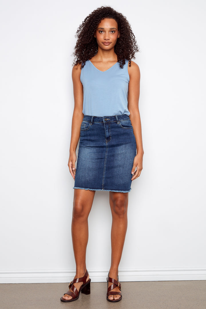 Woman wearing a light blue sleeveless top and denim skirt against a white background