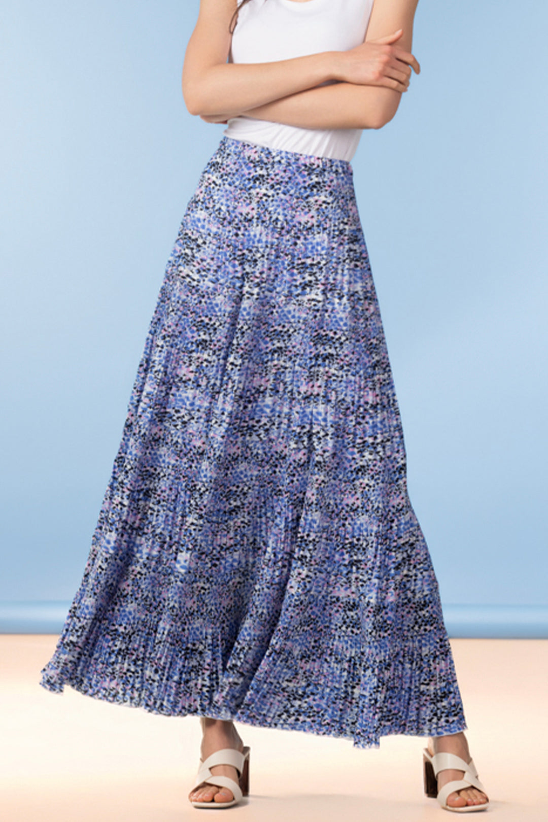 Person wearing a blue patterned long pleated skirt with a white top against a light blue background.