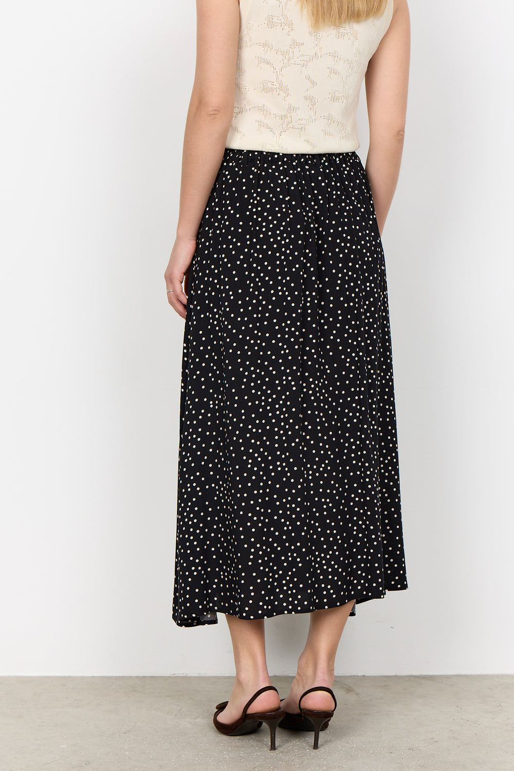 woman wearing a black midi skirt with white polka dots on a white background.