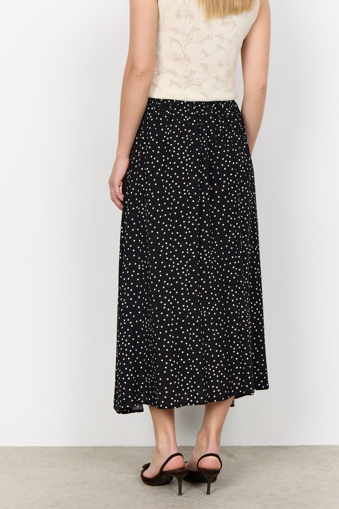 woman wearing a black midi skirt with white polka dots on a white background.