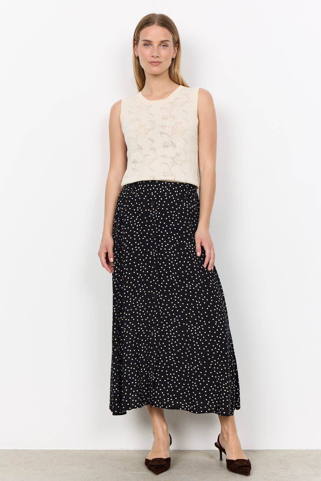 woman wearing a cream blouse with a black midi skirt with white polka dots on a white background.