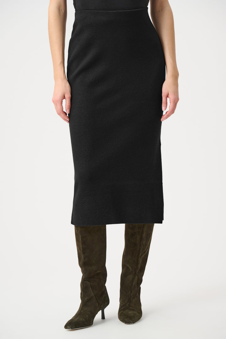 Person wearing a black pencil skirt with green high-heeled boots on a white background