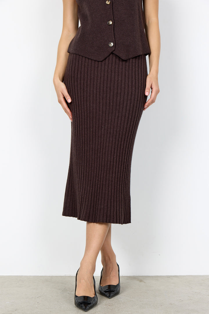 A model wearing a dark brown ribbed knit midi skirt paired with a matching dark brown button-front vest and black pointed-toe heels, set against a plain white studio background.