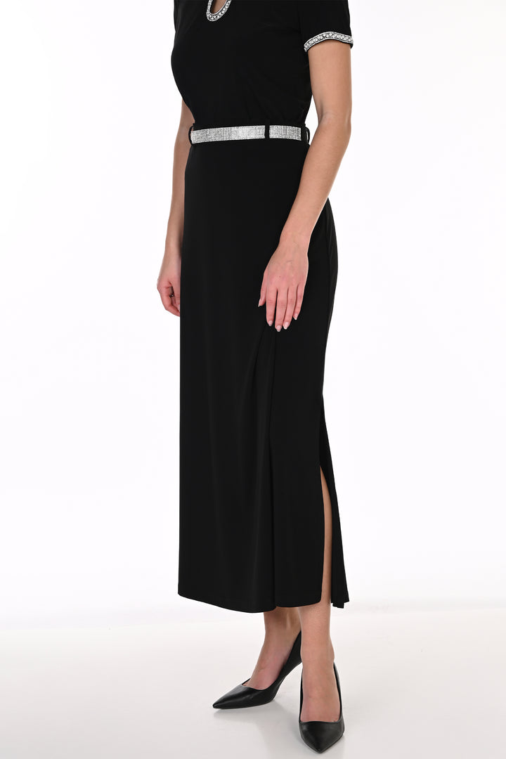 A woman modeling a black short sleeve top, midi skirt with a high slit, and a silver embellished belt, paired with black pointed-toe heels against a white studio background.