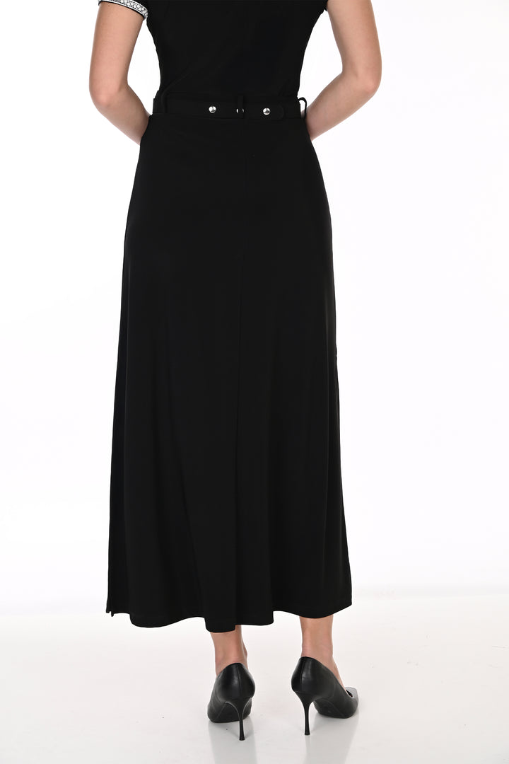 A woman modeling a black top, midi skirt with a high slit, and a silver embellished belt, paired with black pointed-toe heels against a white studio background.