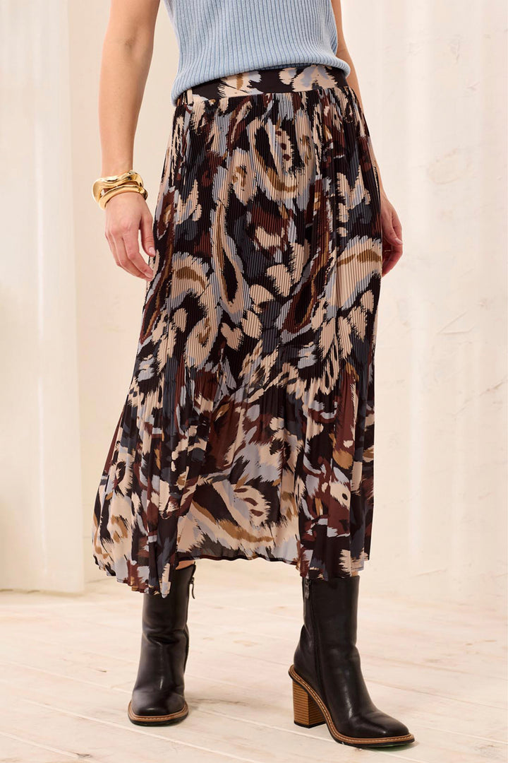 A woman wearing a brown and beige printed textured shirt and black boots standing in front of a beige background. 