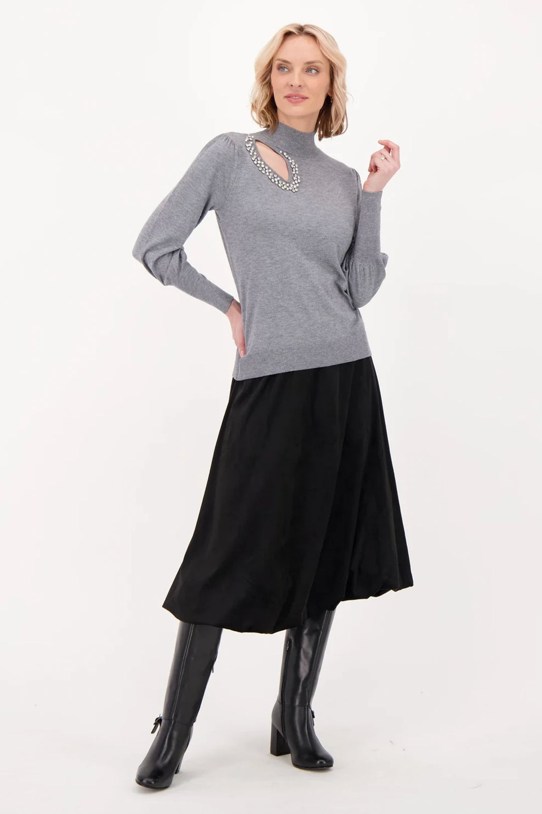 A woman wearing a long black suede skirt over black boots standing in front of a grey background. 
