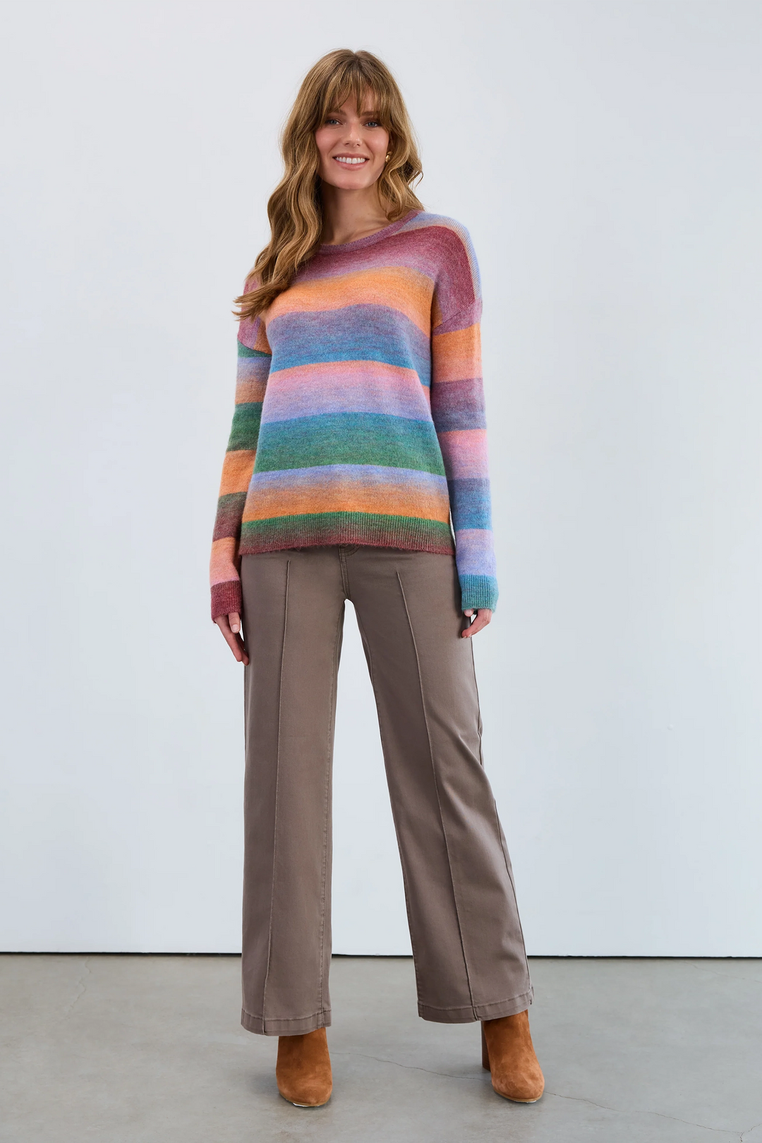 Woman wearing a colorful striped sweater and brown pants against a white background
