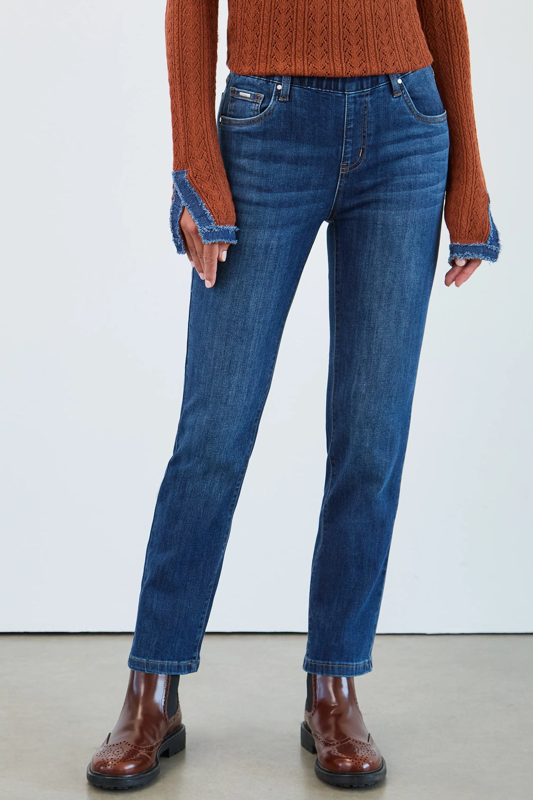 Person wearing blue jeans and a rust-colored sweater on a white background